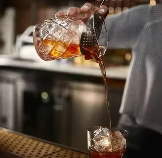 Bartender pours amber drink from mixing glass into a second glass.