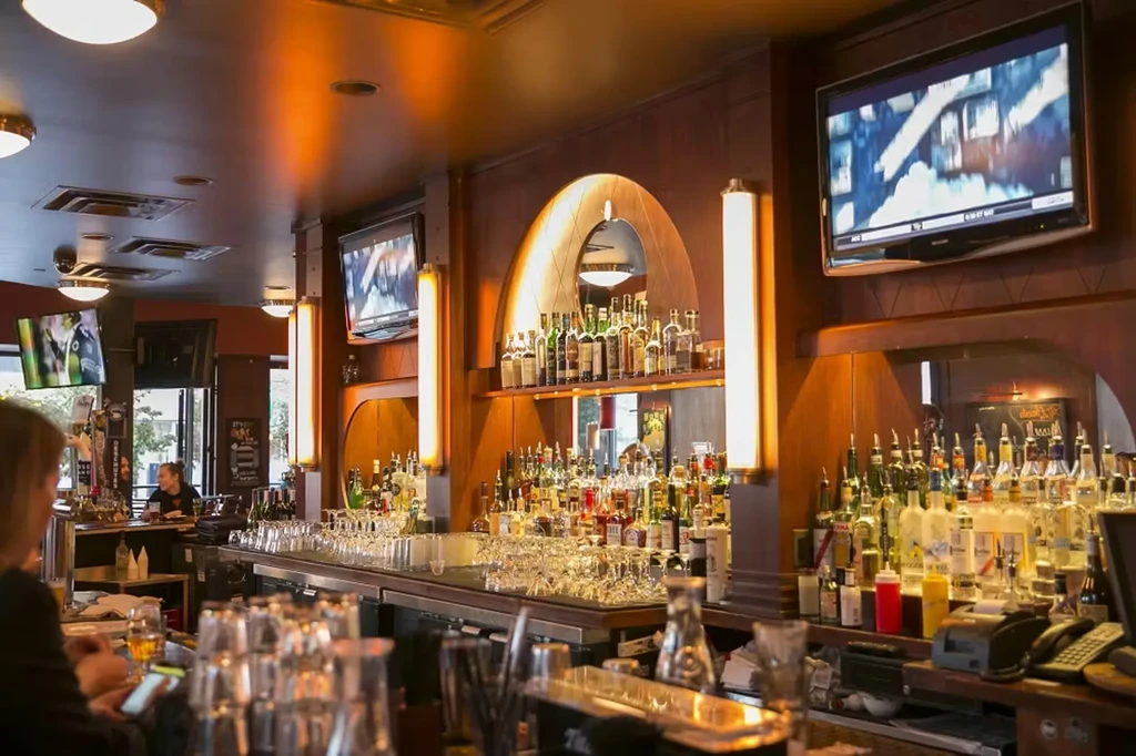 Interior of a well-stocked bar with spirits, glasses, and TVs.