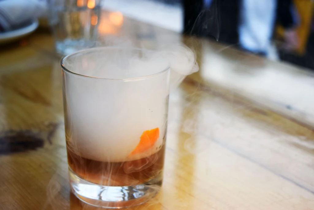 Close-up of a smoking drink with orange peel on a wooden table.