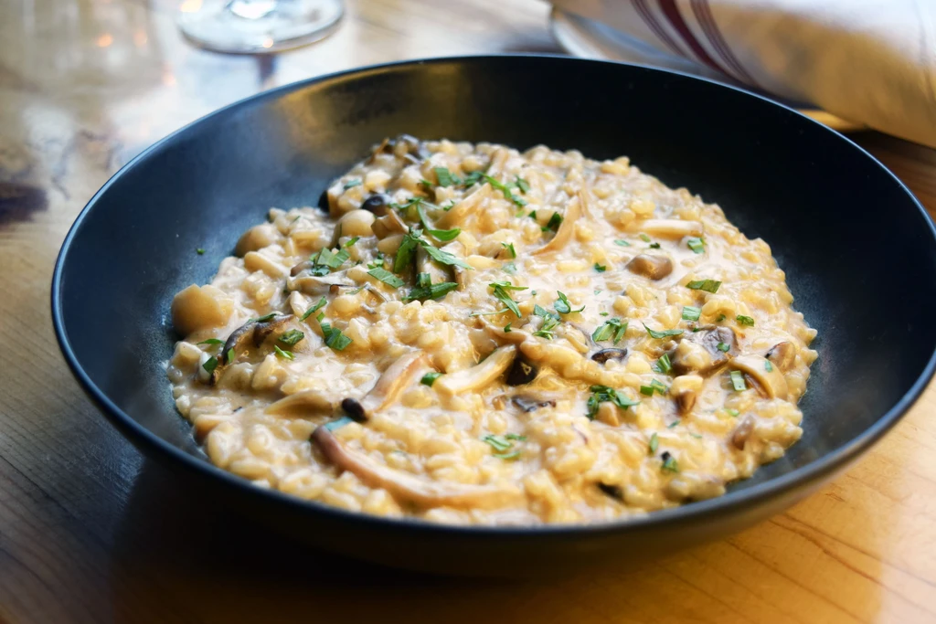 Creamy mushroom risotto in a black bowl, garnished with green herbs.