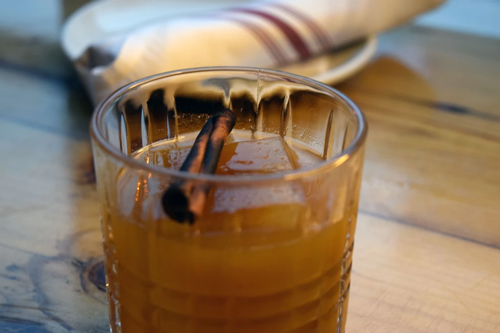 Amber drink with ice and cinnamon stick in a textured glass.