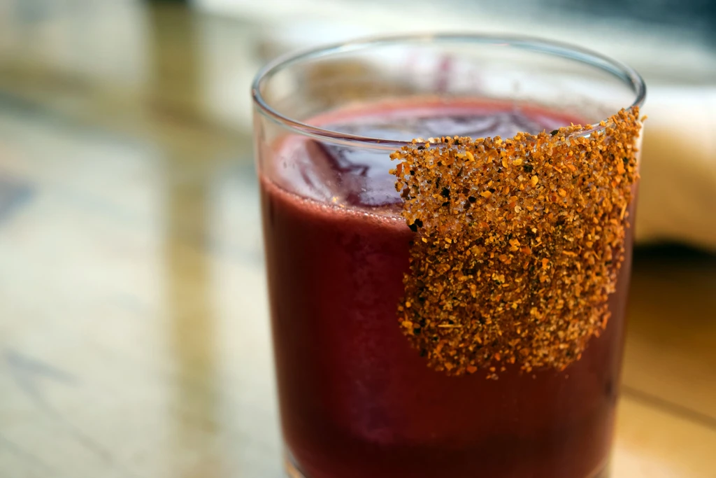Dark red beverage in a clear glass with a seasoned rim.
