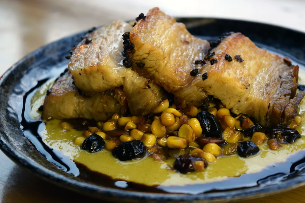 Three pieces of seared meat on corn, green sauce, and dark drizzle.