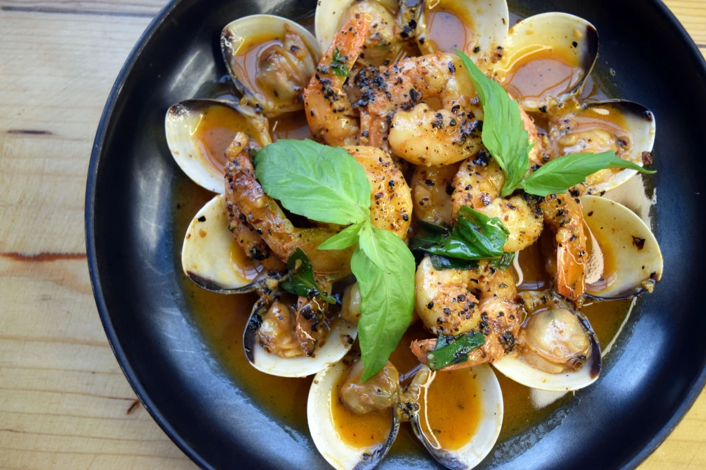 Overhead shot of seasoned shrimp and clams in a black bowl.