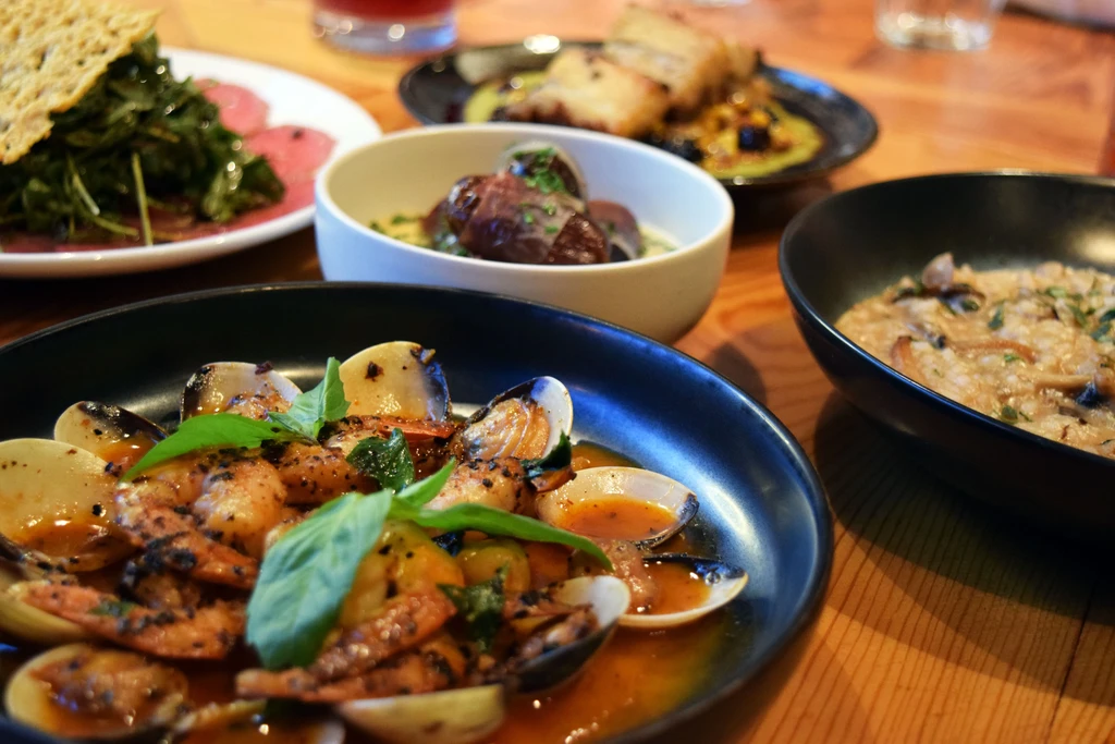 Multiple gourmet dishes: shrimp and clams, carpaccio, dates, and risotto.