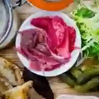 Overhead shot: thinly sliced raw meat, greens, and blurred ingredients on wood.