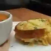 Tomato soup, grilled cheese sandwich, and chips on a white plate.