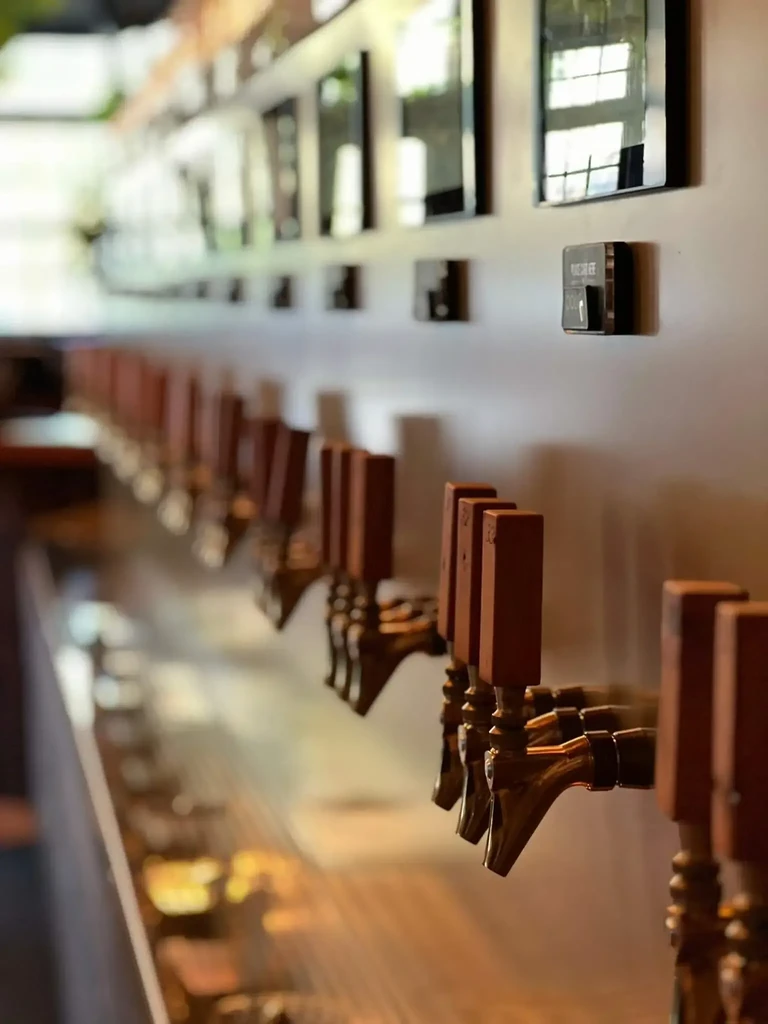 Long row of bronze beverage taps with reddish-brown handles.