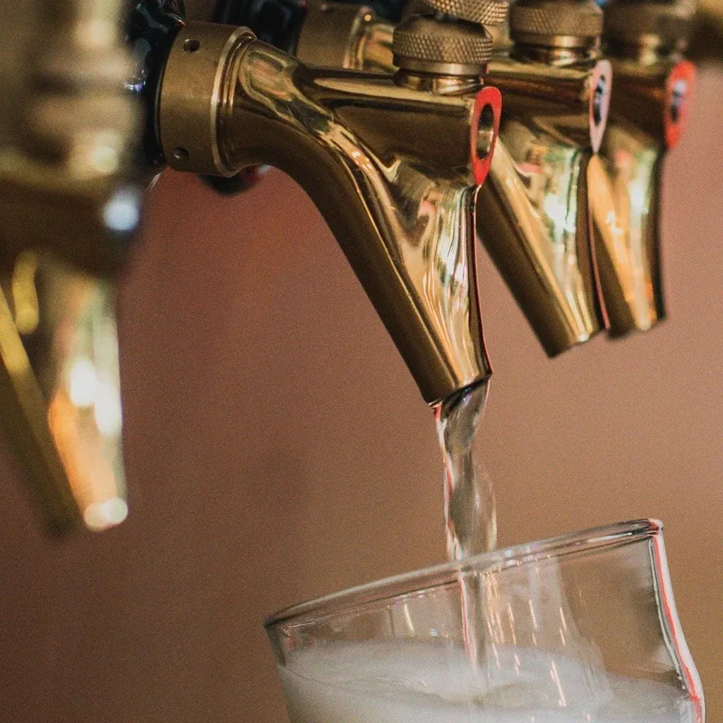 Close-up of golden beer taps, one pouring light liquid into a glass.