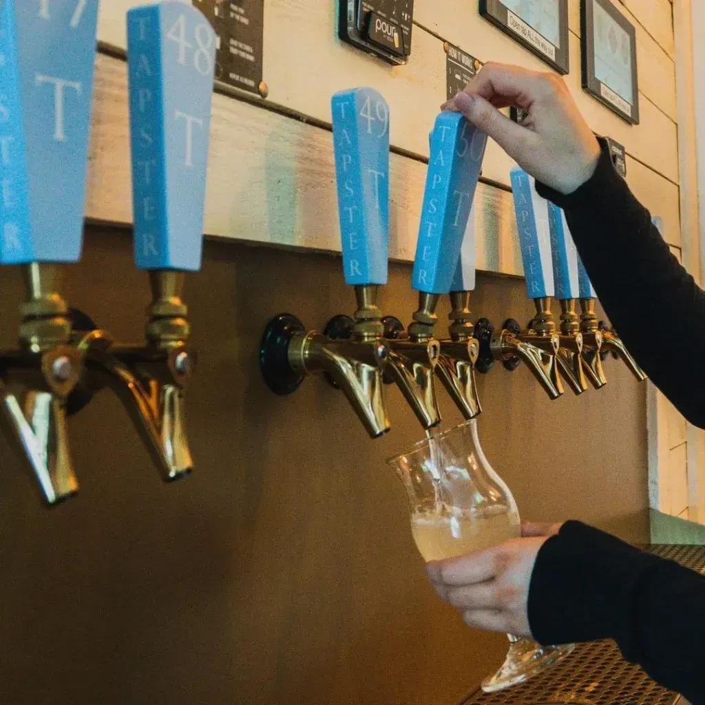Hands pouring a frothy beverage from a beer tap.