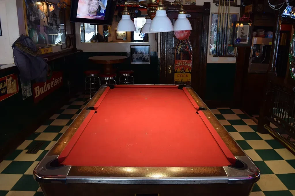 Red-felted pool table in a dimly lit bar with checkerboard floor.
