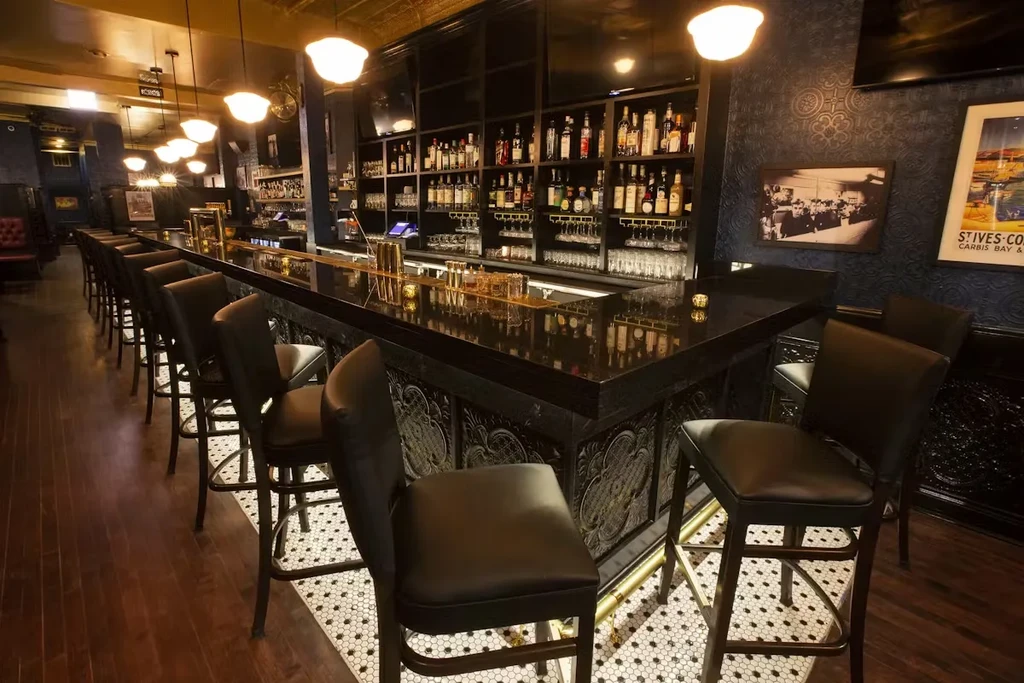 Interior view of a well-stocked bar with warm lighting and hexagon tiles.