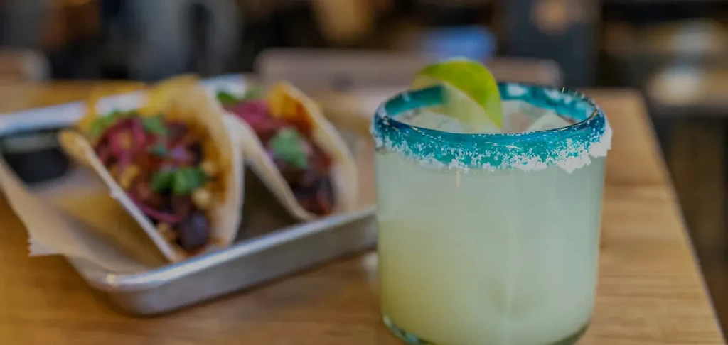 Margarita, tacos, and a lime wedge on a wooden table.