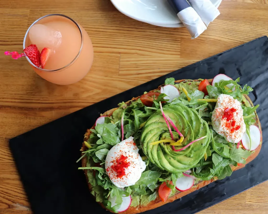 Overhead shot of avocado toast with poached eggs and a frozen drink.