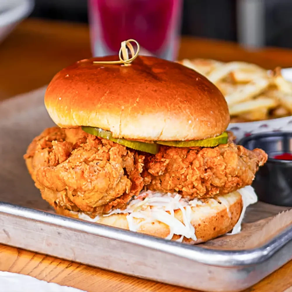 Fried chicken sandwich with coleslaw and pickles on a brioche bun.