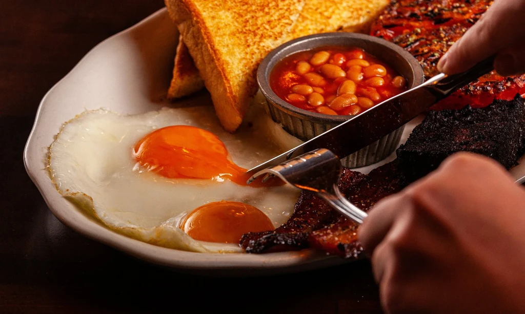 Close-up of a Full English breakfast being cut with a knife and fork.