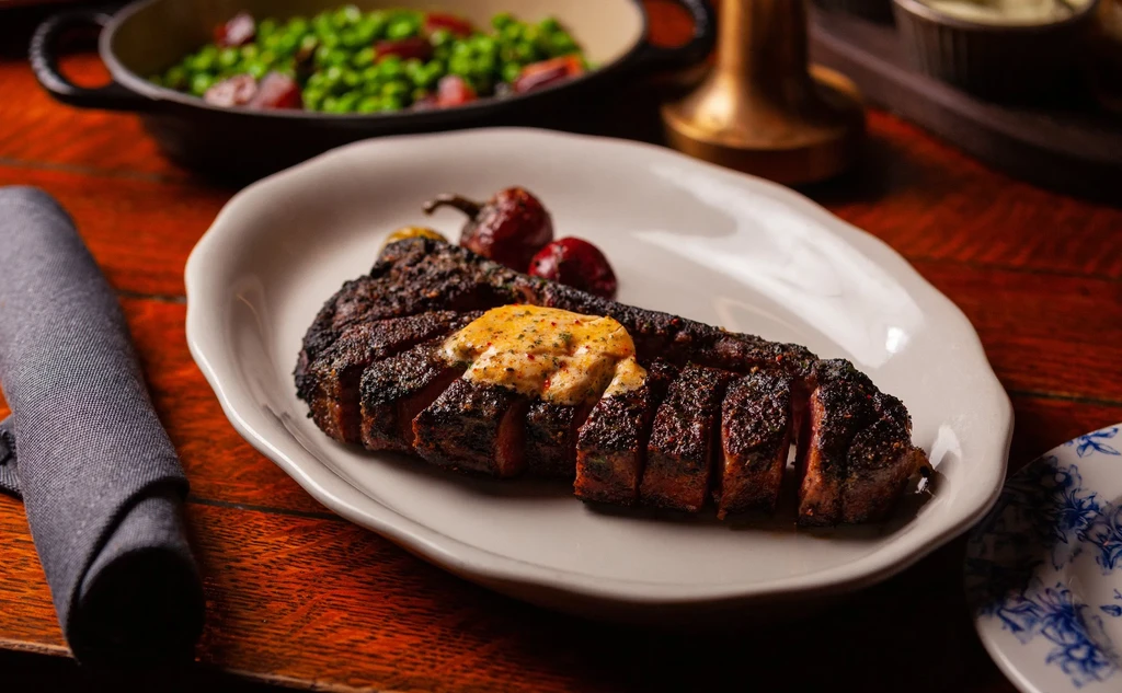 Sliced steak with melting butter, peas, and a floral plate.