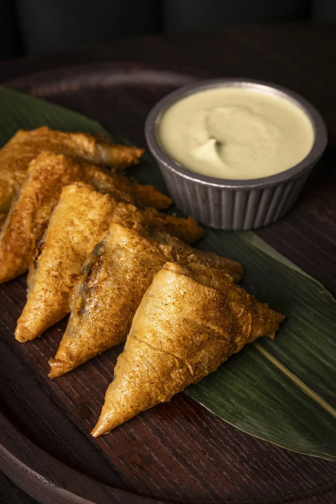 Fried triangular pastries on a leaf with a creamy dip.