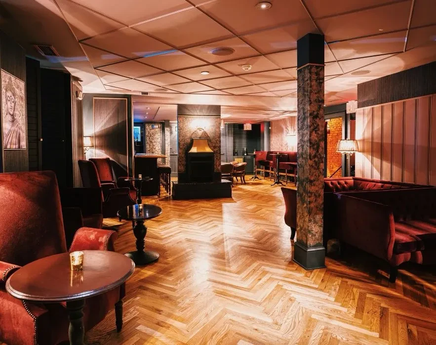 Elegant bar interior with herringbone floor, velvet seating, and decorative column.
