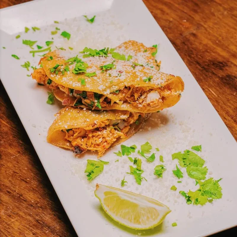 Two golden-brown tacos with cheese, cilantro, and a lime wedge.
