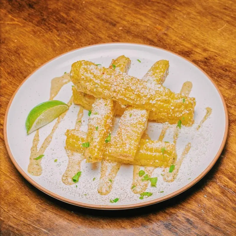 Overhead close-up of corn ribs with sauce, cheese, and a lime.