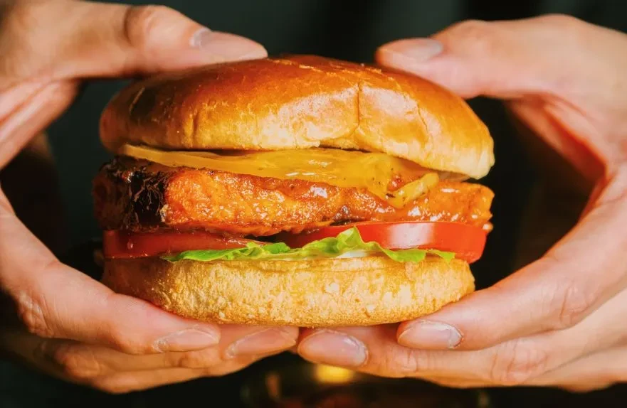Hands hold a gourmet burger with bun, patty, cheese, tomato, lettuce.