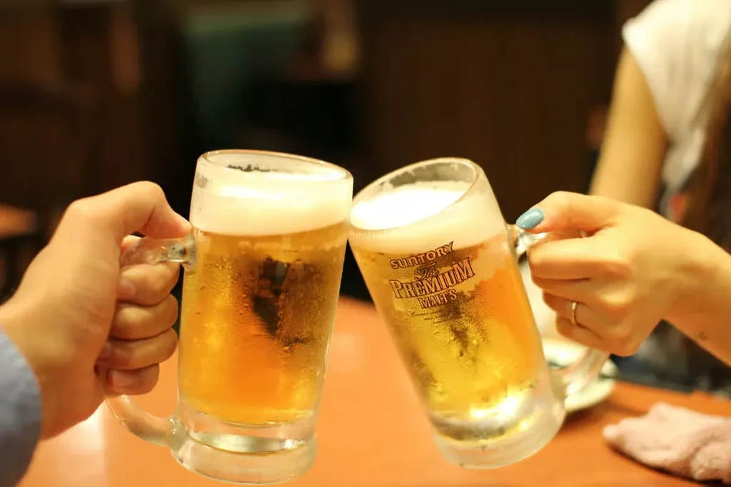 Two hands clink frosty beer mugs of Suntory Premium Malt's.