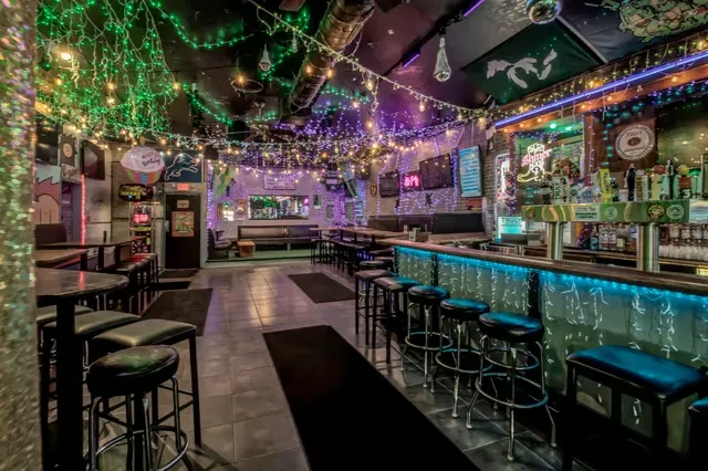 Dimly lit bar decorated with string lights, disco ball, and flags.