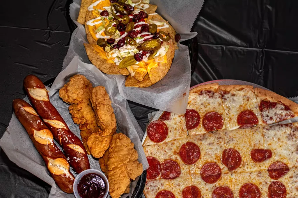 A spread of nachos, pretzels, chicken tenders, and pepperoni pizza.