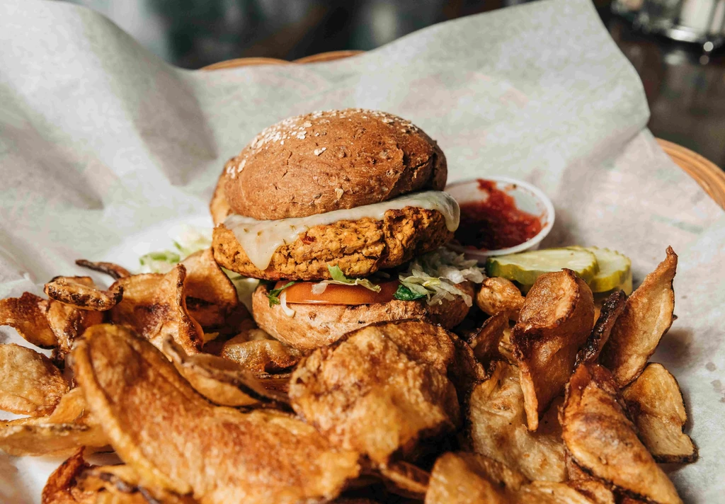 Burger with cheese, lettuce, tomato, chips, and red sauce.
