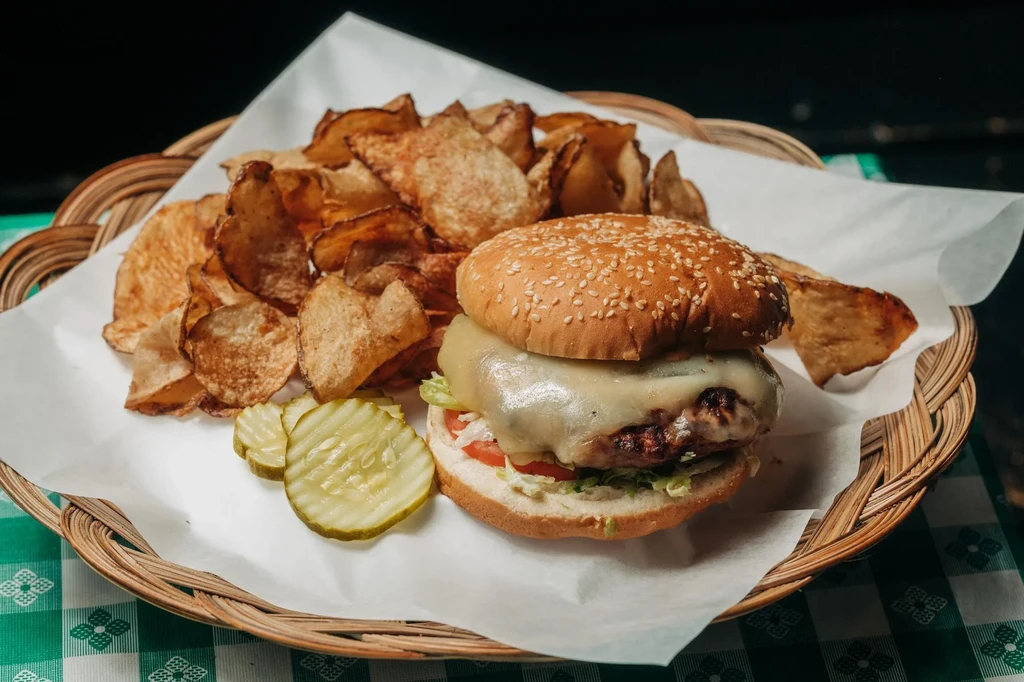 Cheeseburger with pickles and chips in a wicker basket.