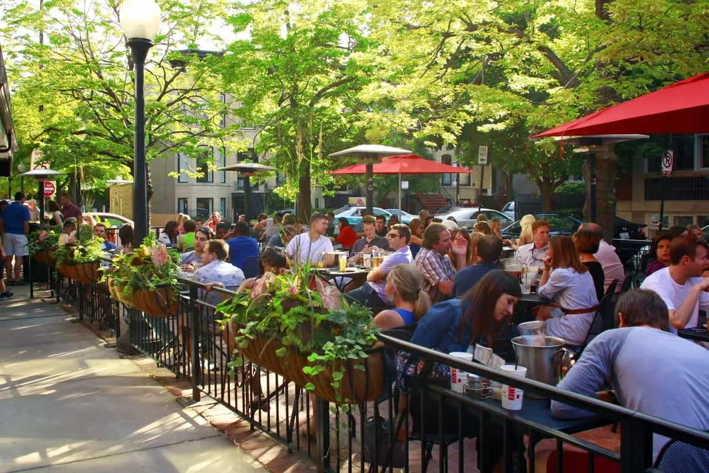 Outdoor restaurant patio filled with people socializing under red umbrellas.