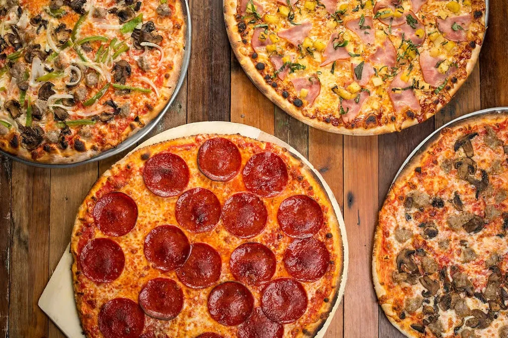 Four freshly baked pizzas with various toppings on a wooden table.