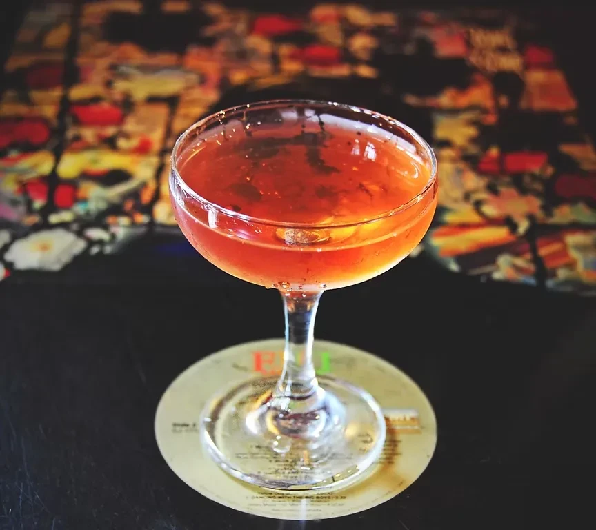 Close-up of an amber cocktail in a coupe glass on a coaster.