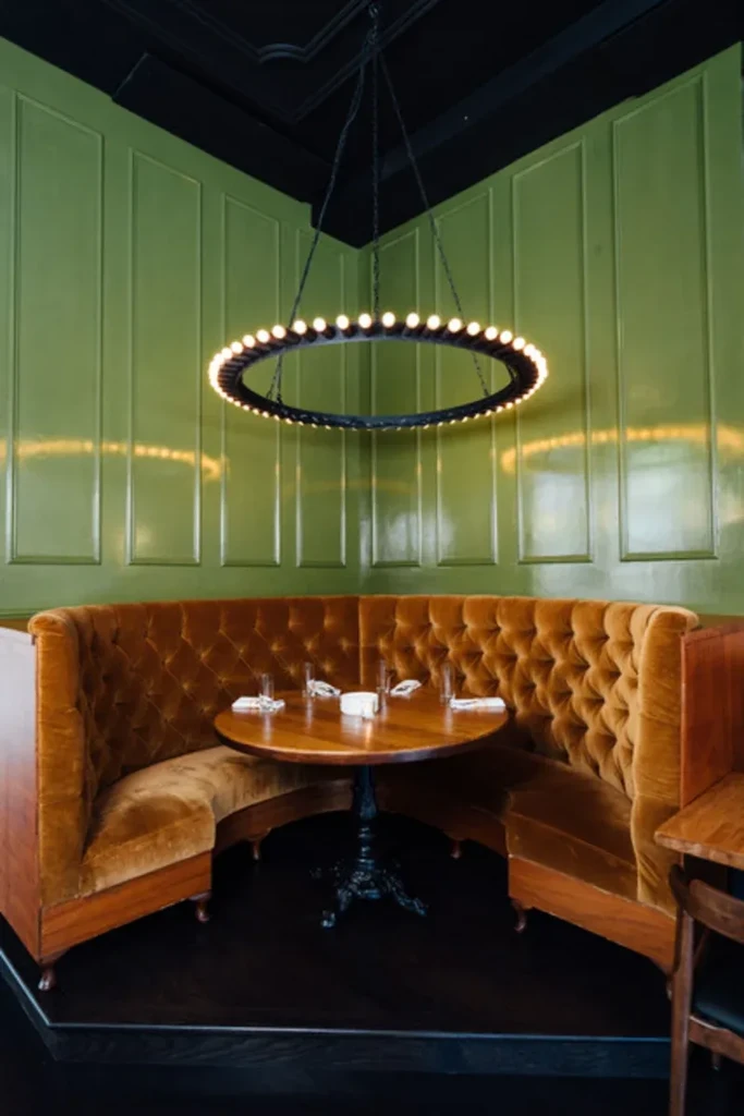 Elegant restaurant interior with an orange-brown booth, round table, and chandelier.