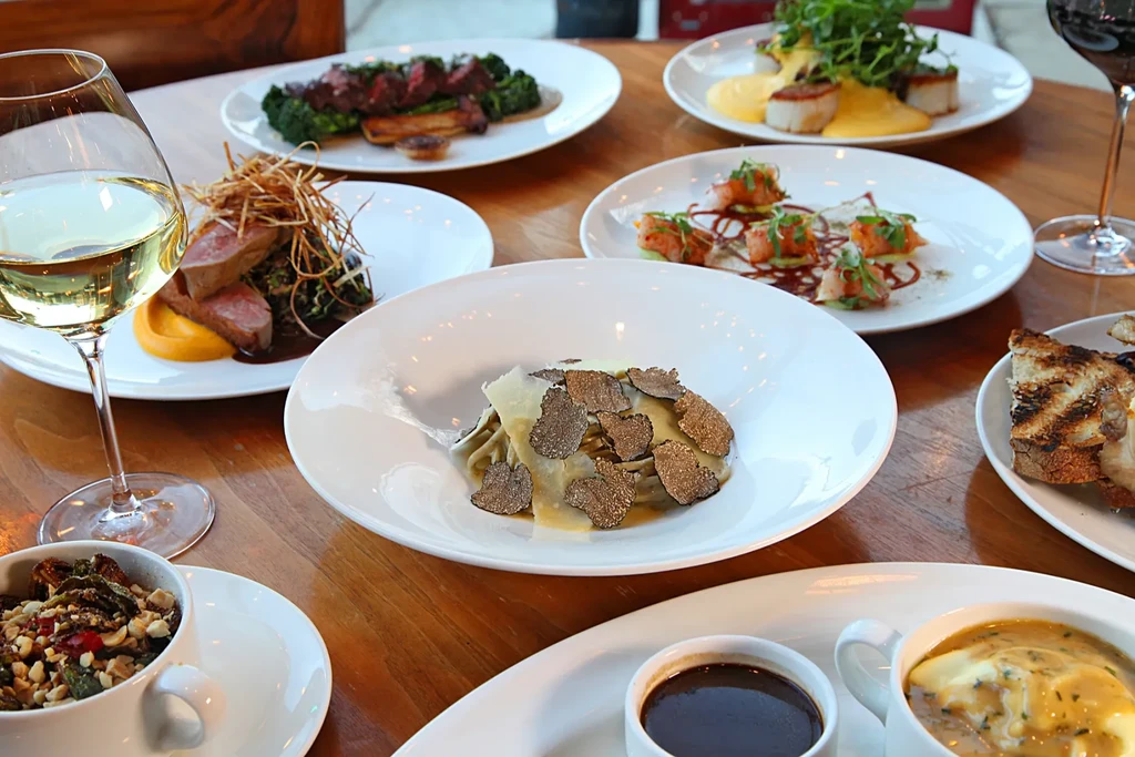 Wooden dining table with pasta, truffles, scallops, duck, and wine.