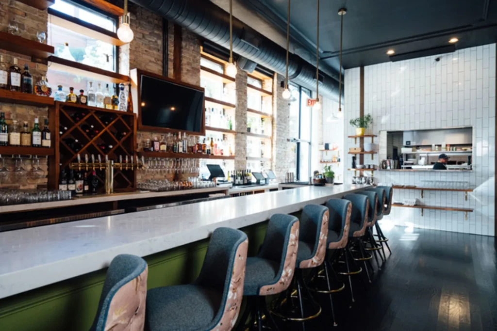 Modern restaurant bar with marble counter, stocked shelves, and brick walls.