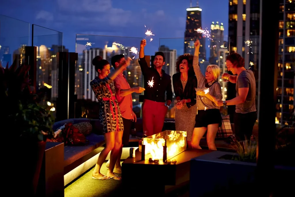 Six people celebrate with sparklers on a city rooftop at night.