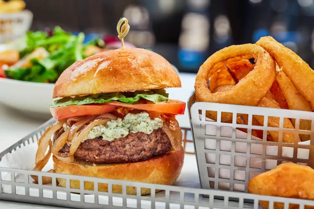 Gourmet burger with blue cheese and caramelized onions, side of onion rings.