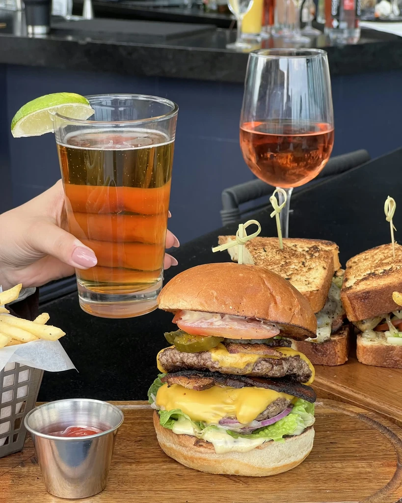 Close-up of a cheeseburger, fries, and beer on a dark table.