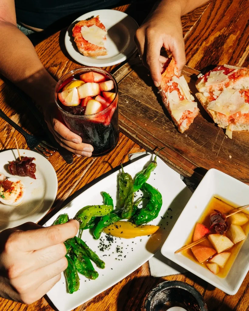 Overhead view of hands sharing tapas and sangria on a wooden table.