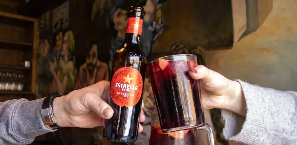 Two people toasting with a beer bottle and a glass of sangria.