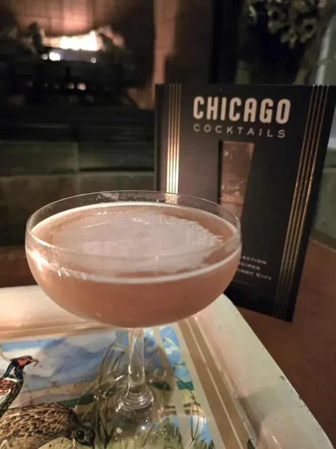 Cocktail in coupe glass on tray; book and fireplace in background.