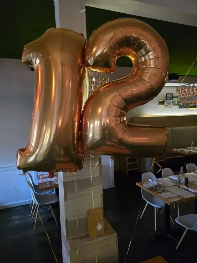 Rose gold number balloons "12" in a restaurant dining area.