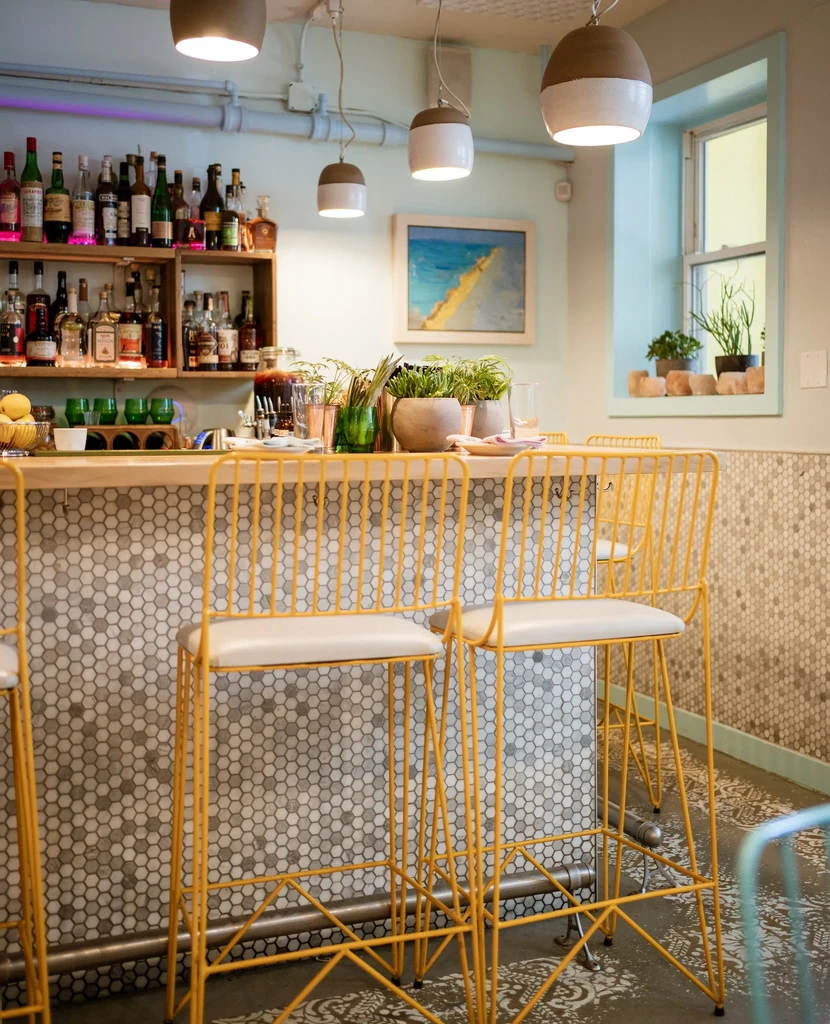 A well-stocked bar with hexagonal mosaic tiles and yellow bar stools.