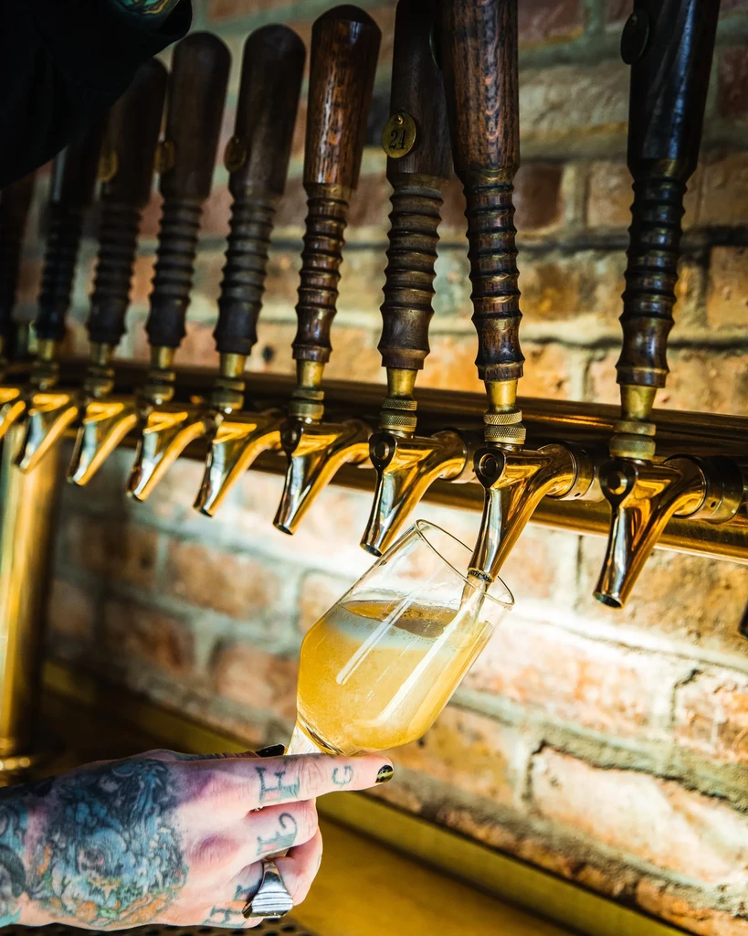 Hand holding a glass, pouring beer from golden taps.