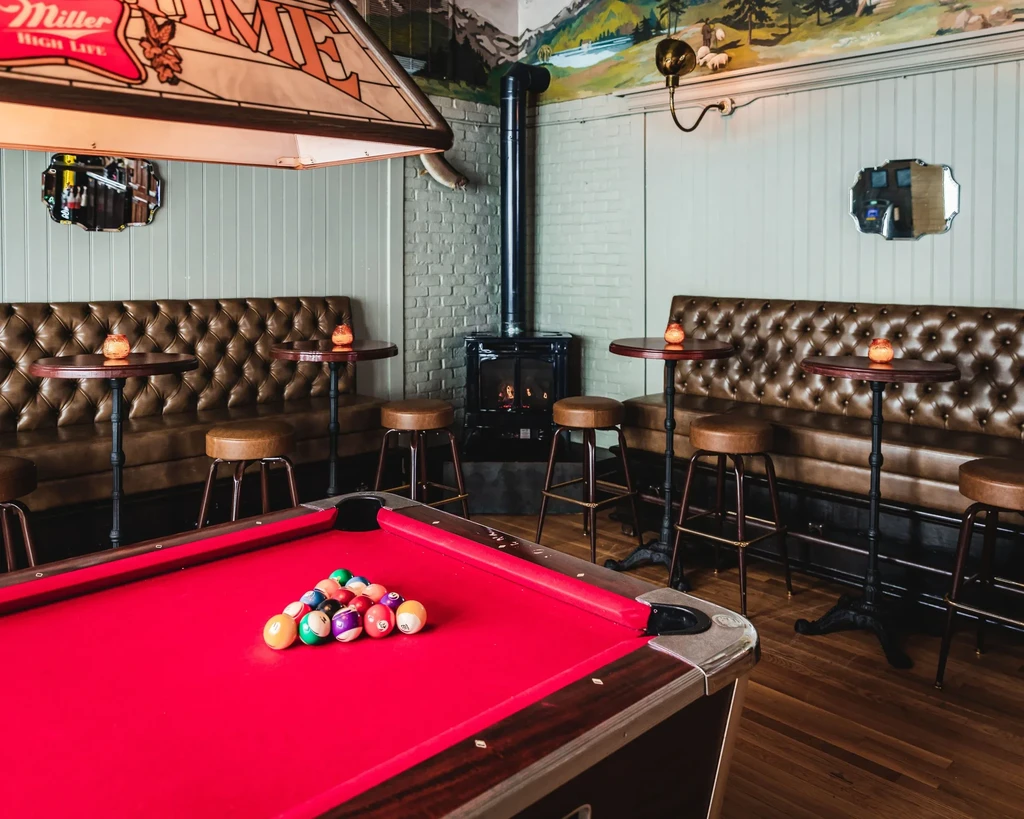 Red felt pool table in a dimly lit bar with seating.