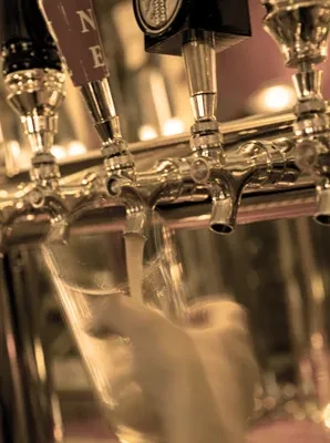 Close-up of beer taps, one pouring light beer into a glass.