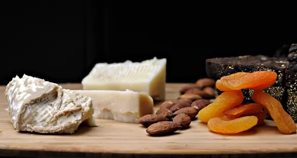 Close-up of cheese, almonds, and dried apricots on a wooden surface.