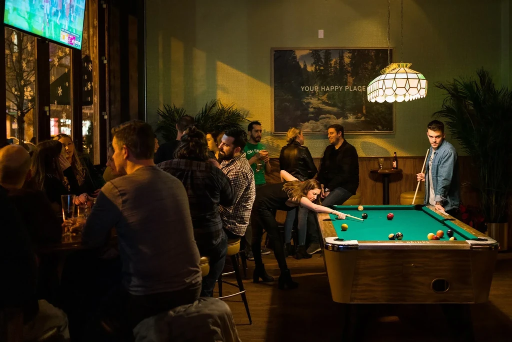 People play pool and socialize in a dimly lit bar.